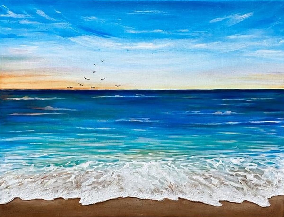 A wave breaking in thick white foam on brown sand, a calm blue sea and a pale orange horizon with a few birds.